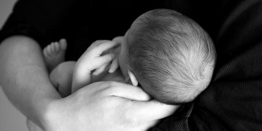 Snugglebundl - Importance of Supporting a Baby’s Head Blog - Black and white image of a father holding his new born baby